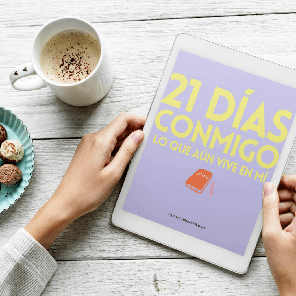 Una mano sosteniendo una tablet que muestra la portada de un libro titulado '21 DÍAS CONMIGO LO QUE AÚN VIVE EN MÍ', junto a una taza de café y un plato con galletas.
